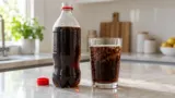 Garrafa genérica de refrigerante aberta ao lado de um copo com bolhas visíveis.