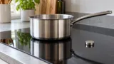 Panela de aço sobre fogão de indução de vidro em uma cozinha doméstica