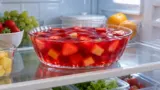 Tigela de gelatina vermelha com frutas dentro da geladeira